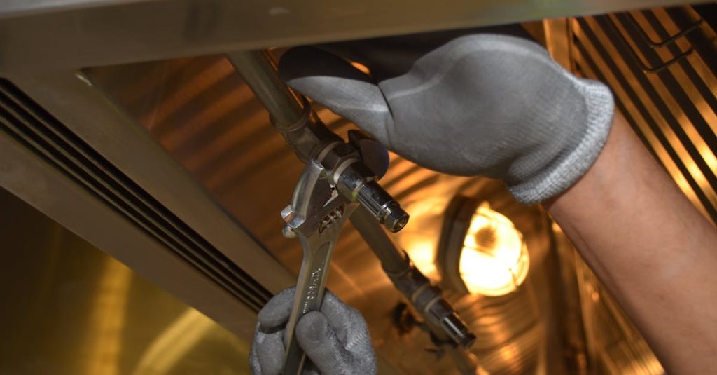 A worker fixing pipes with tools in an industrial indoor environment.